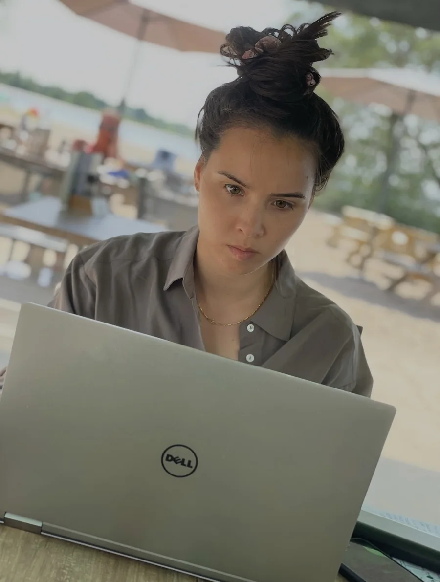 Eline werkt geconcentreerd achter een laptop op een terras aan het water.