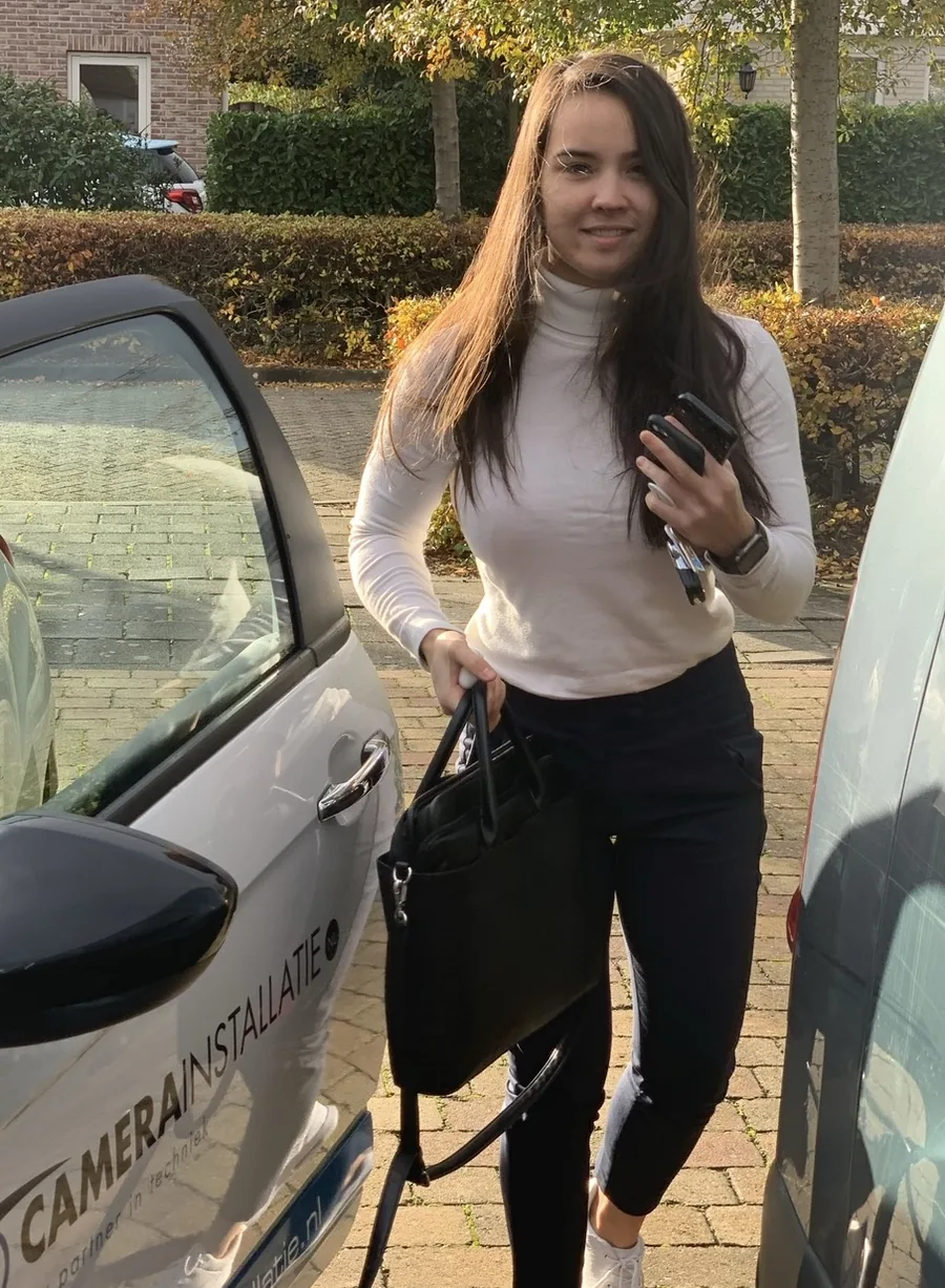 Eline stapt uit een bedrijfsauto, tas in de ene hand, telefoon in de andere, herfstlicht.