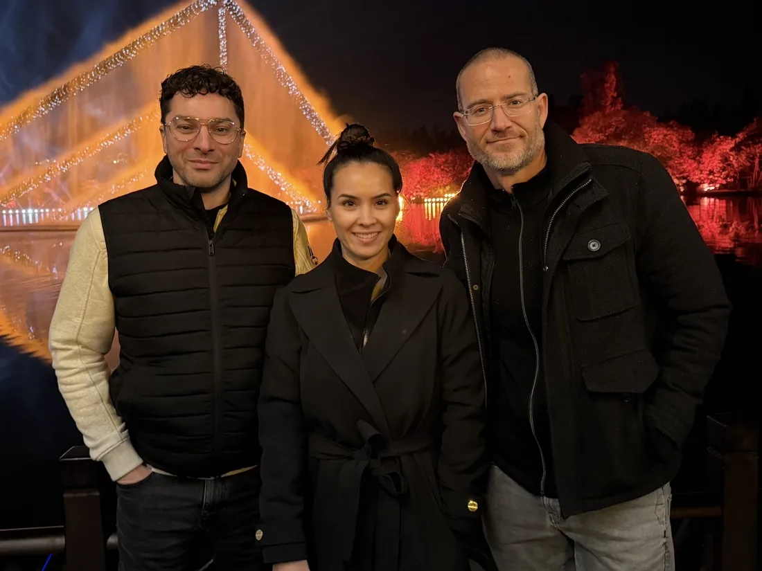 Marc Herdes, Eline Klaver en John van den Bosch naast elkaar, 's avonds buiten voor een verlichte fontein.