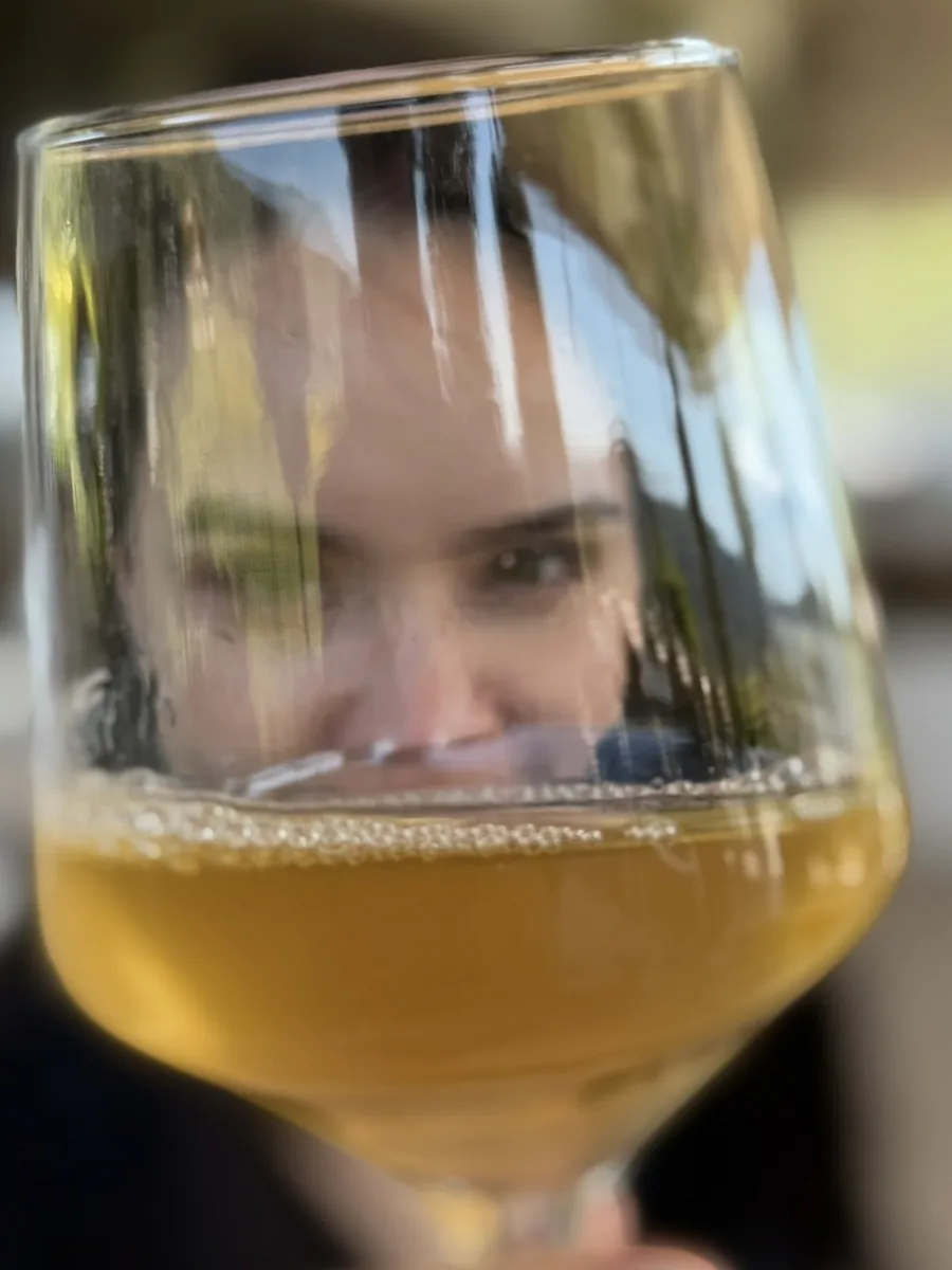Eline kijkt door een wijnglas heen in de camera.