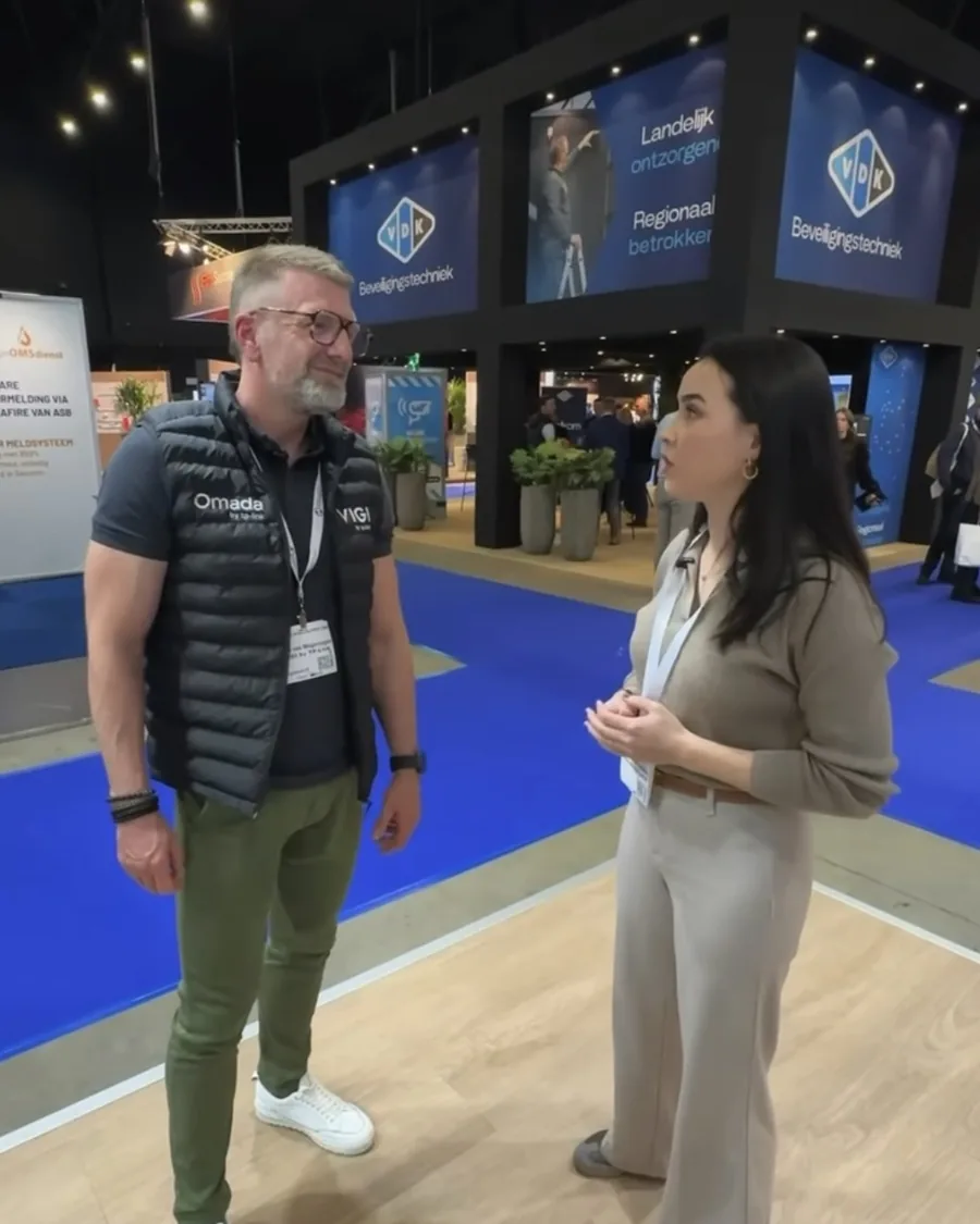 Eline interviewt een man op de beursvloer; hij praat, zij luistert.