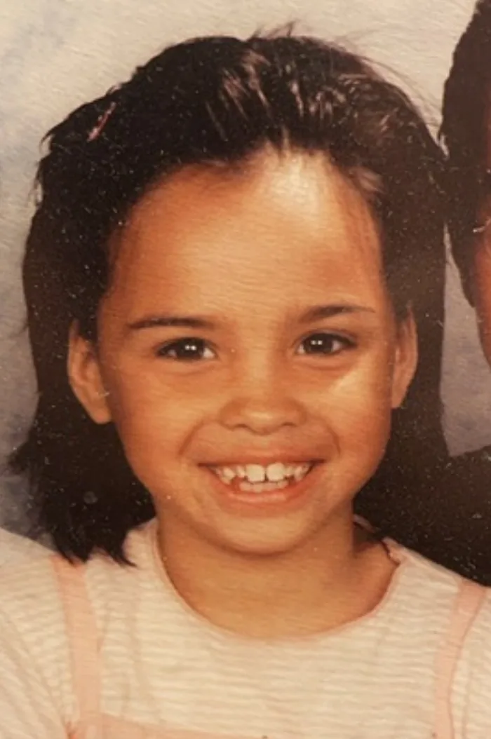 Eline als klein meisje op een schoolfoto, breed lachend.