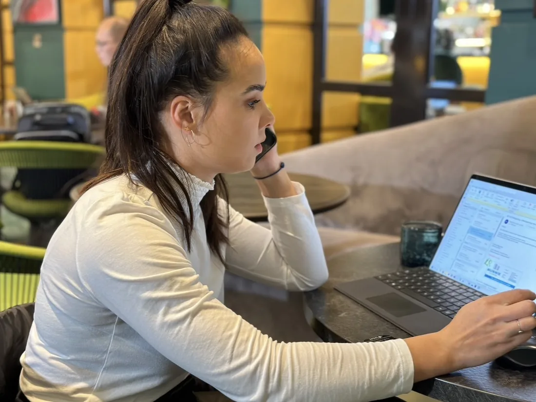 Eline en profil, werkend achter de laptop, hand bij haar gezicht, in een lounge.
