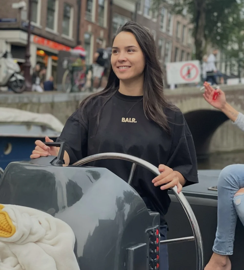 Eline aan het roer van een boot in een Amsterdamse gracht, lachend.