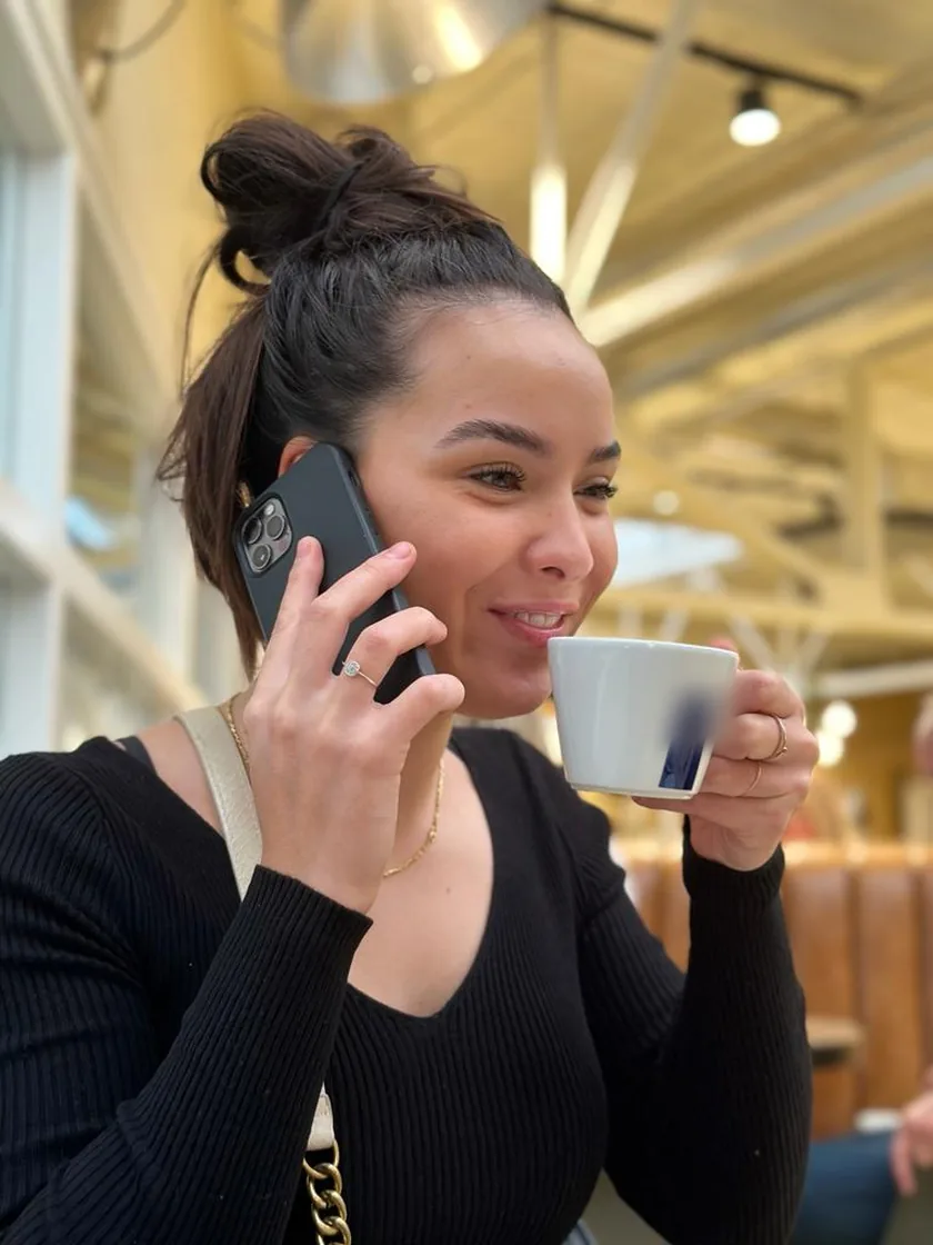 Eline aan de telefoon met een kopje koffie, lachend.