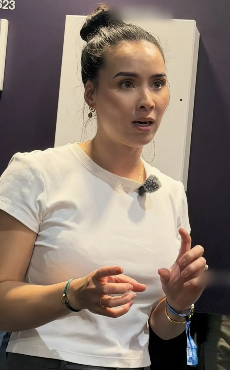 Eline vertelt op een beursstand, midden in een zin, handen erbij, een dasspeldmicrofoon op haar shirt.