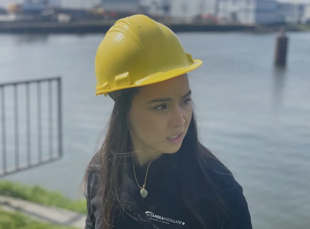 Eline op een kade, gele helm, het water achter haar.